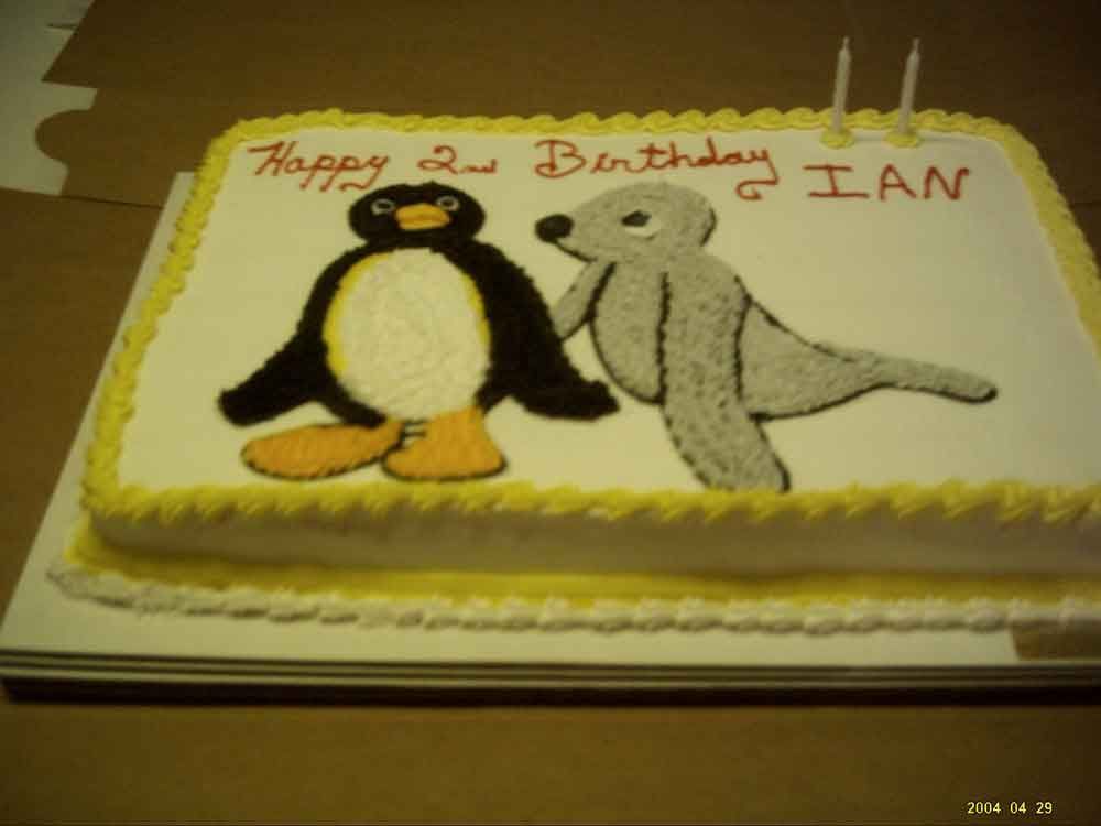 Cake decorated with cartoon penguin and seal, yellow icing border, text 