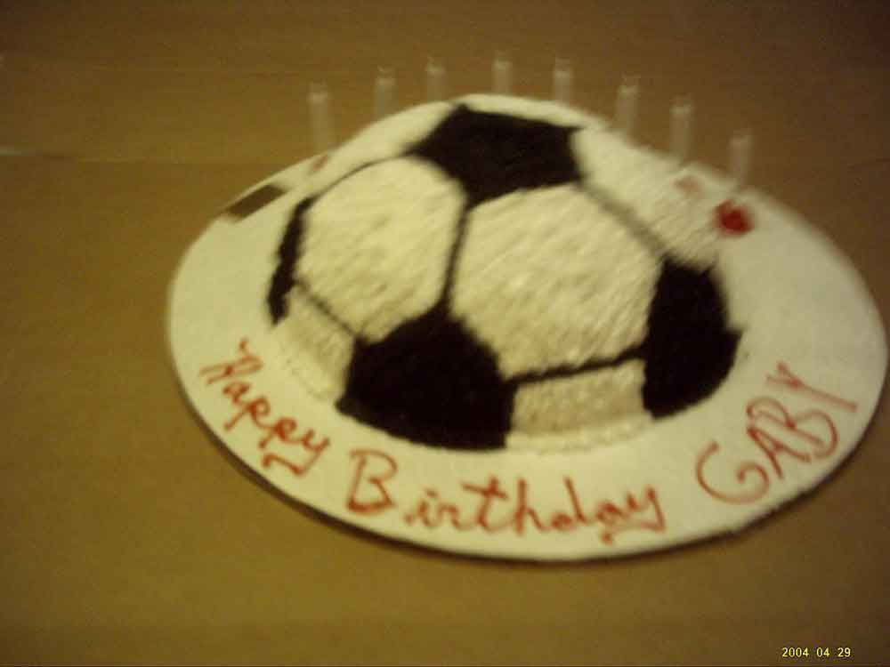 Soccer ball-shaped birthday cake with black and white icing, white frosting border, 