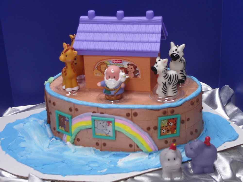 Cake decorated as Noah's Ark with animal figurines and a purple-roofed toy ark on a blue wave-like frosting.