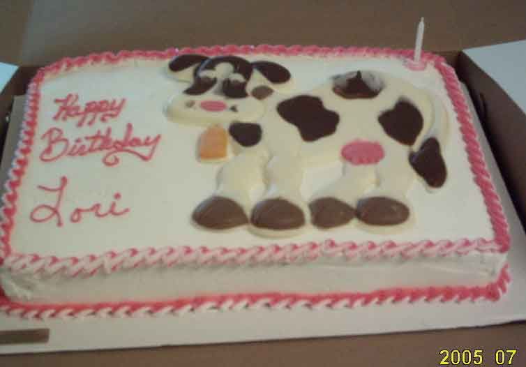 Birthday cake decorated with a cow design and “Happy Birthday Lori” in pink frosting.