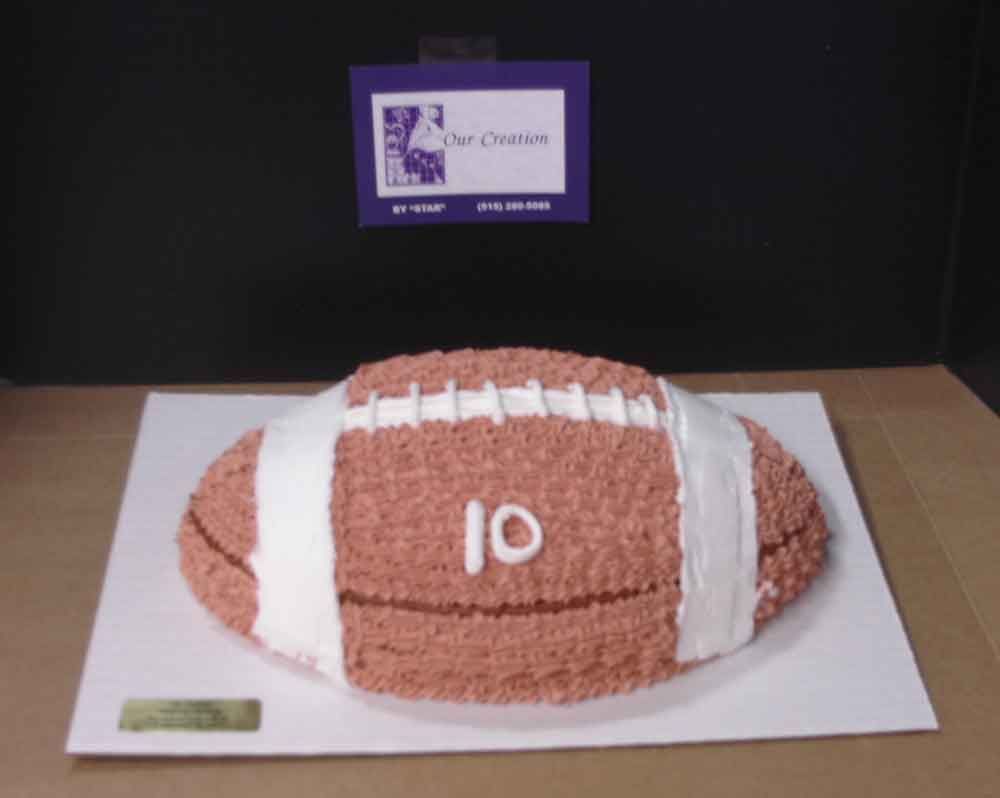 Football-shaped cake, brown frosting with white stripes and number 10, displayed on white board.