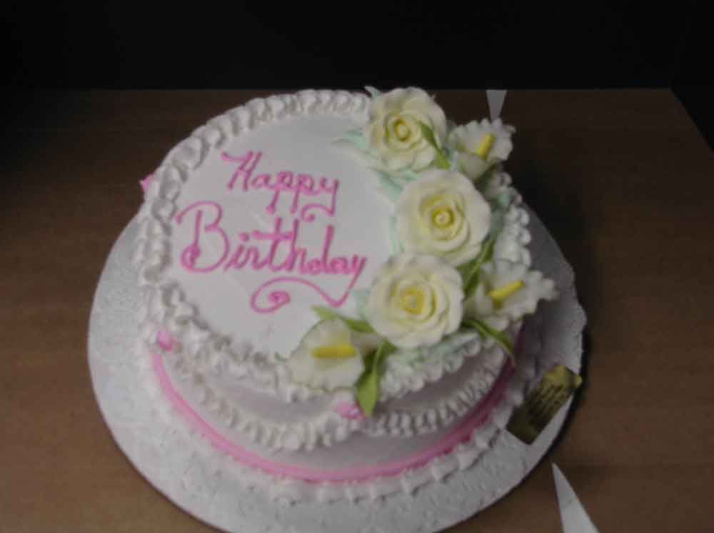 Birthday cake with white frosting, pink accents, and flower decorations.