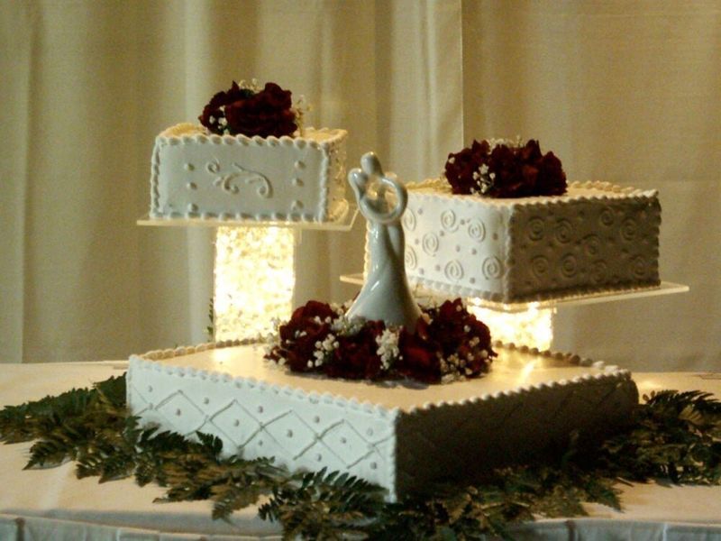 Three-tiered wedding cake, decorated with red flowers and white icing. A bride and groom topper stands on the middle tier.