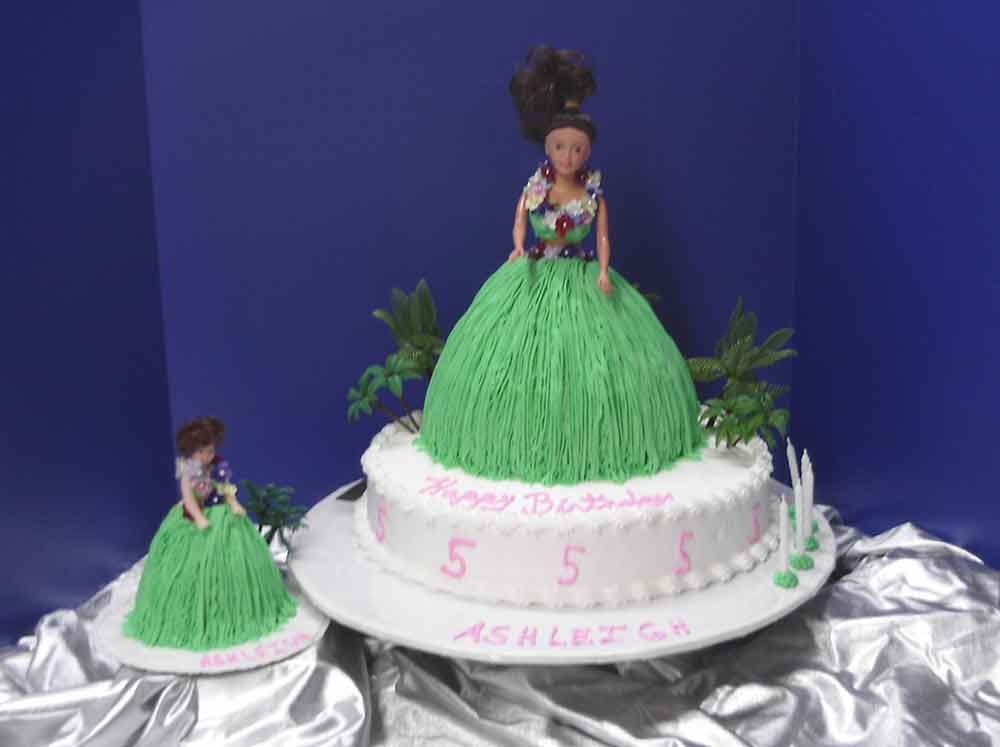 Two-tiered cake with a doll on top and a smaller cake. Green skirt design. 