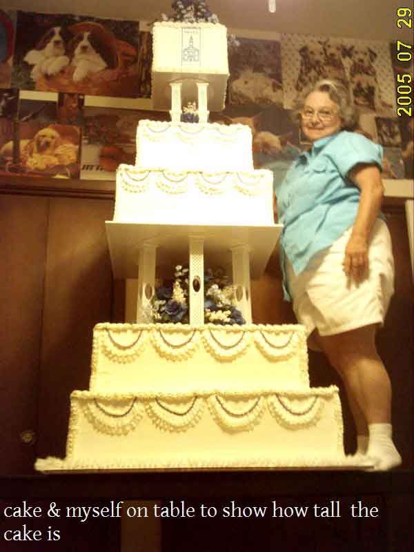 Woman standing next to a very tall, multi-tiered white cake, on a table; July 29, 2005.