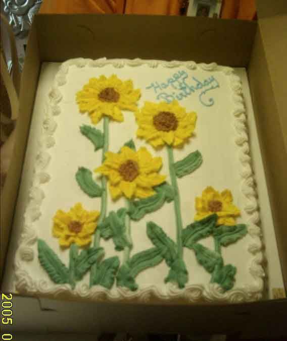 Birthday cake decorated with yellow frosting sunflowers and green leaves, in a box.