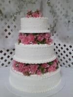 Four-tiered white cake, decorated with pink flowers, on a white cake stand.