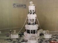 Five-tiered white wedding cake with floral decorations, surrounded by smaller cakes and greenery.
