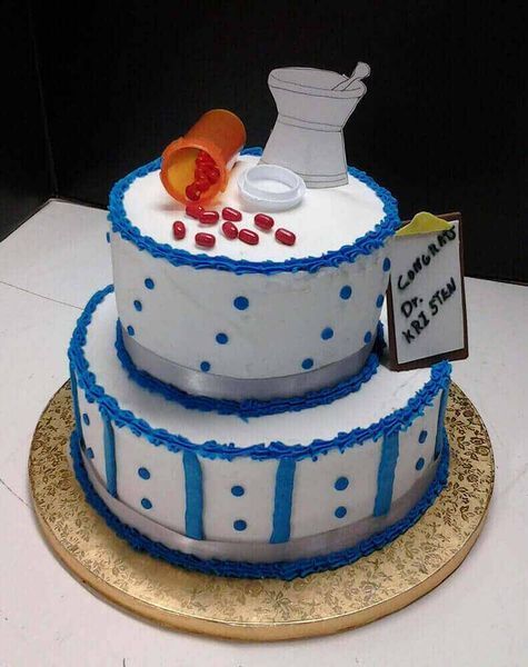 Two-tiered cake decorated as a pharmacist's office, with pills, mortar and pestle, and a congrats sign.
