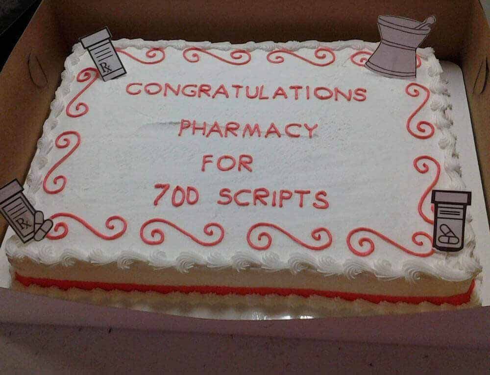 Cake celebrating pharmacy for 700 scripts, decorated with red frosting and pill bottle cutouts.