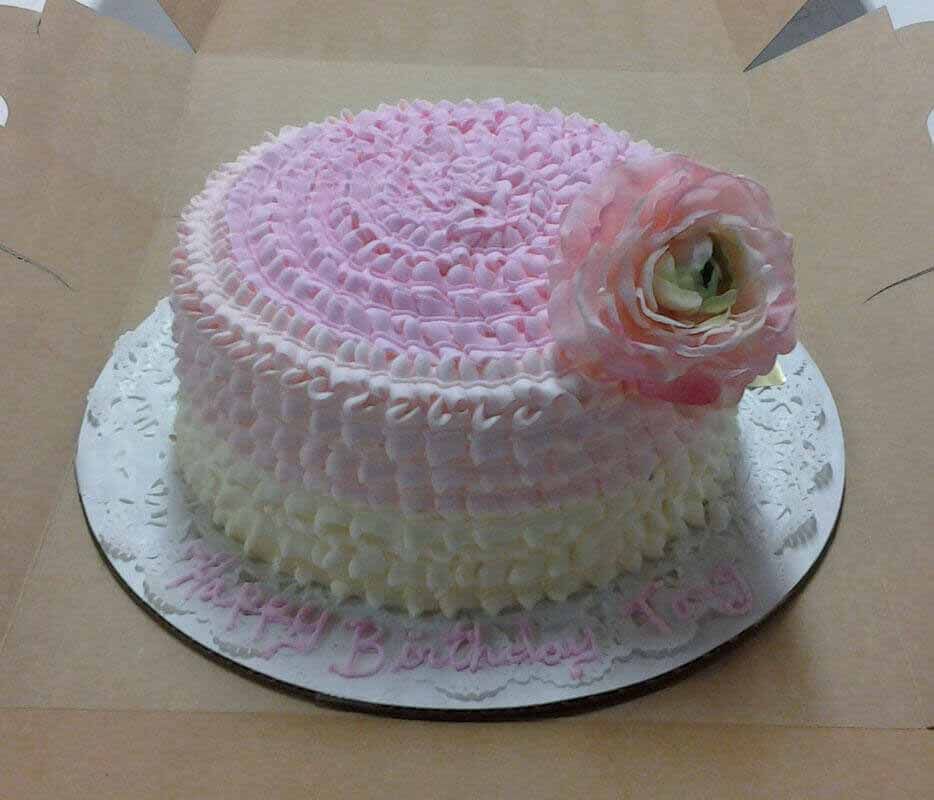 Pink and white frosted cake with a floral decoration, on a doily.