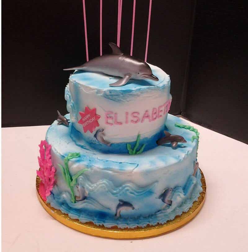 Two-tiered cake with blue frosting, dolphins, and pink name 