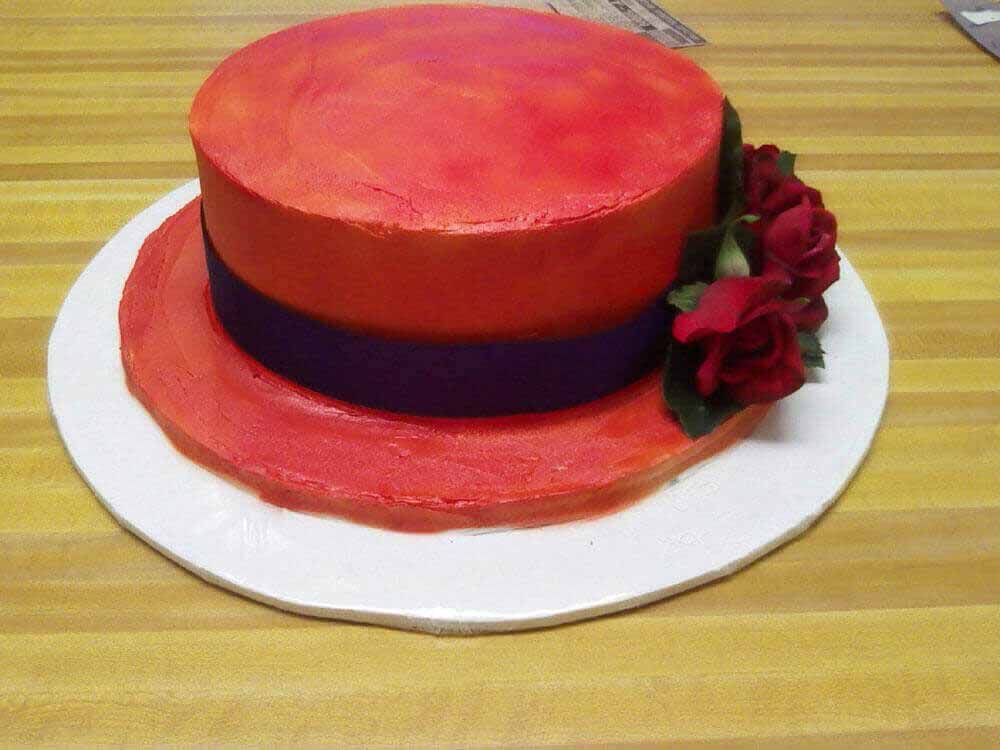 Cake in the shape of a red hat with a purple band, decorated with red roses.