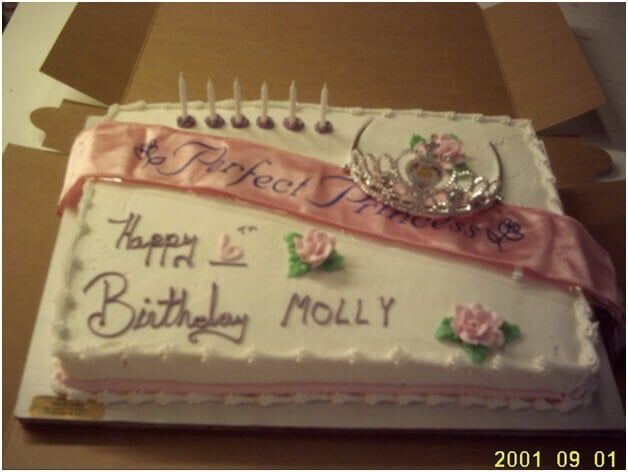 Rectangular birthday cake with pink sash, tiara, roses, candles, and inscription 
