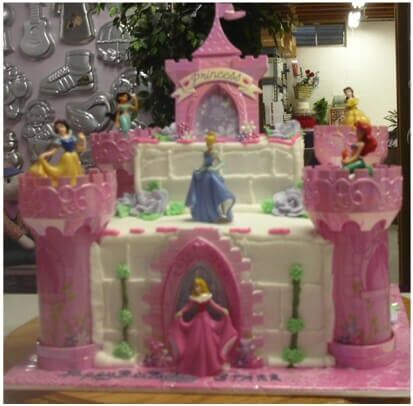 Princess castle cake with Disney figurines. Pink and white with green accents.