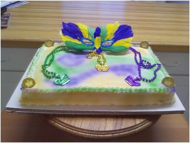 Mardi Gras cake decorated with mask, beads, and coins in purple, green, and yellow on a wooden surface.