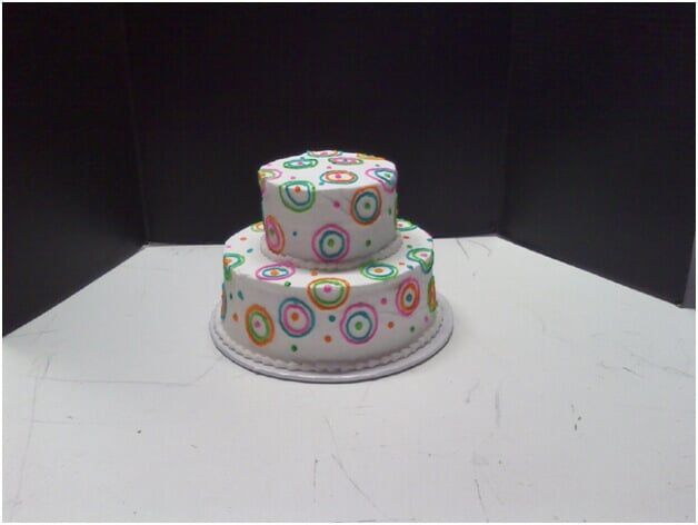 Two-tiered white cake decorated with colorful concentric circle pattern on a white surface with a black background.