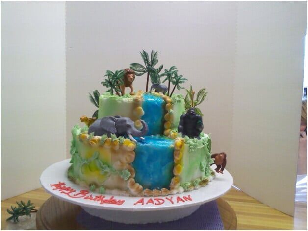 Two-tiered jungle-themed birthday cake with waterfall, animals, and 