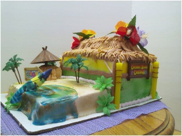 Island-themed cake with a hut, water, sand, palm trees, and flowers; 