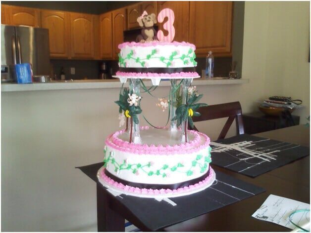 Three-tiered birthday cake with pink frosting, green vines, and 