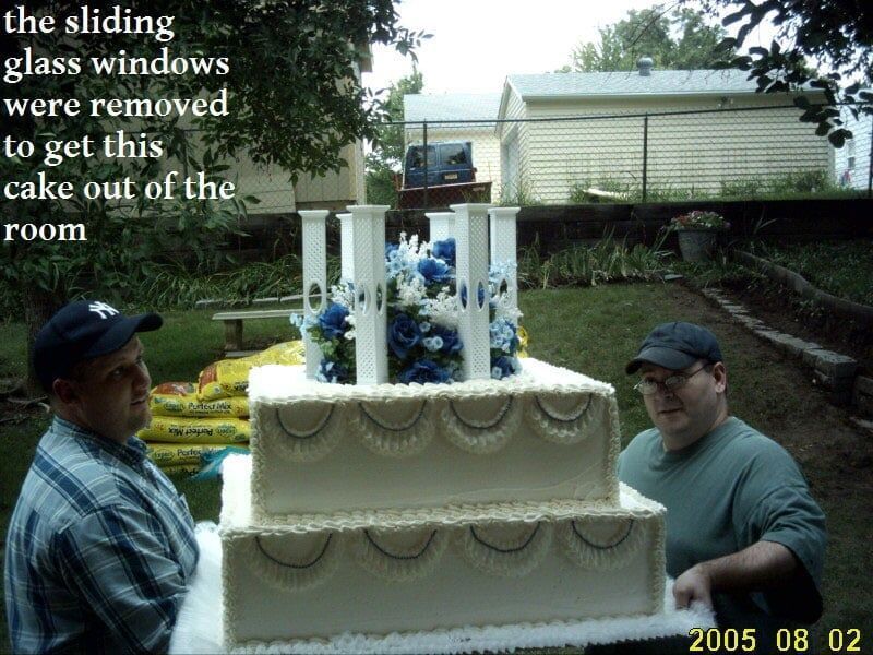 Two men carrying a large tiered cake outdoors. Text says windows removed to get cake out.