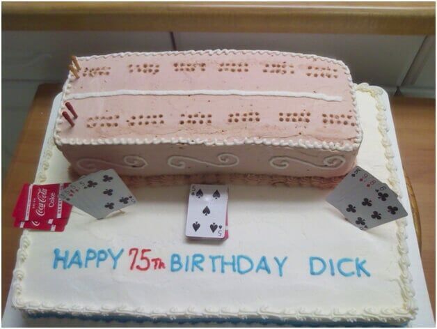 Cake decorated for a 75th birthday, with a cribbage board and playing cards on top. Reads 