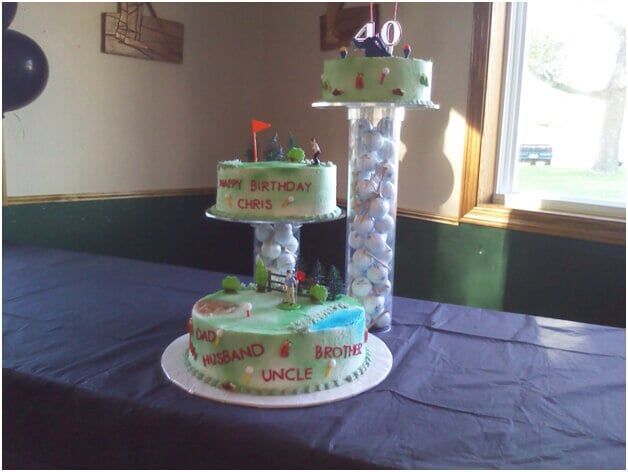 Three-tiered golf-themed birthday cake on table with golf balls inside a clear support column.