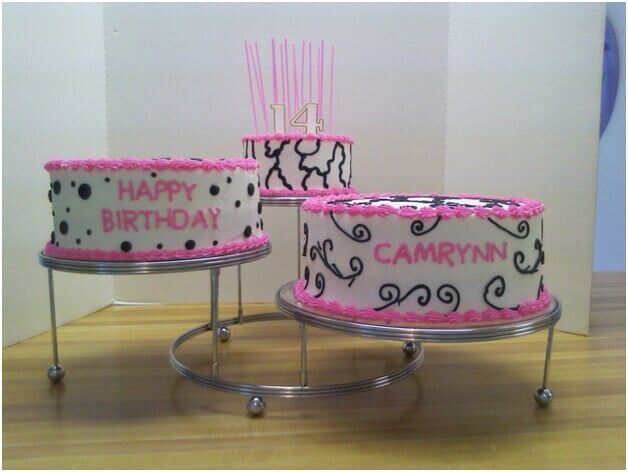 Three tiered birthday cakes on stands, decorated in pink and black.