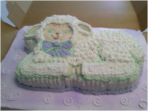Lamb-shaped cake, frosted in white, with light green and lavender accents, lying down in a box.