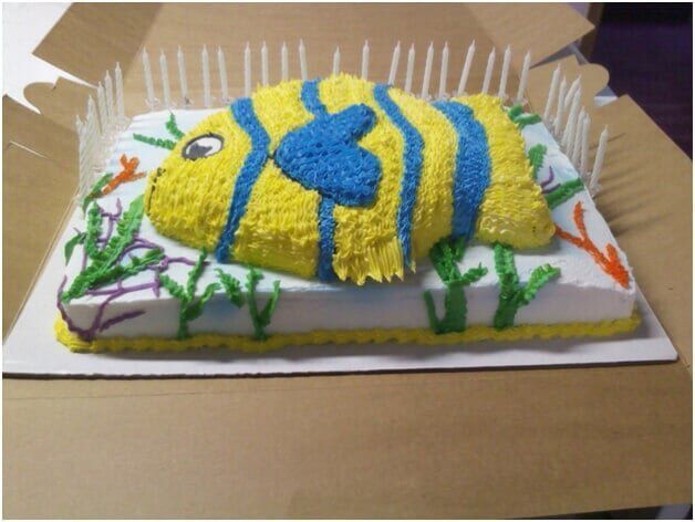 Fish-shaped cake decorated with yellow and blue frosting, candles around it.