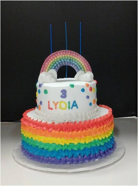Two-tiered rainbow cake with rainbow frosting, rainbow-shaped topper, and 