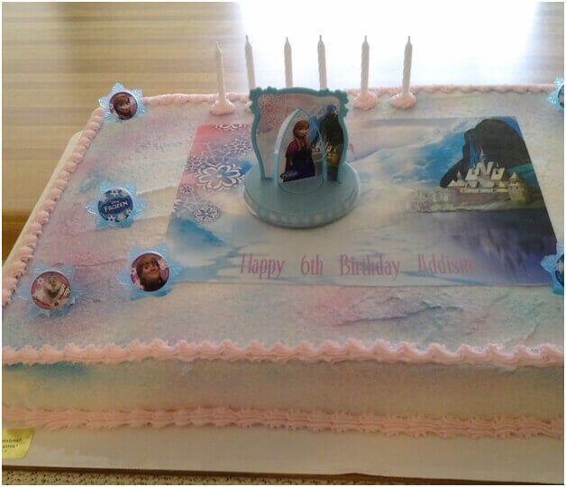 Frozen-themed birthday cake with candles, blue and pink frosting, and character decorations.