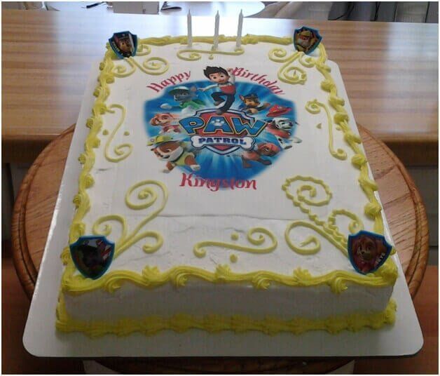 Birthday cake decorated with Paw Patrol logo, yellow frosting, candles, and “Happy Birthday Kingston” text.