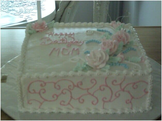 White frosted cake decorated with pink flowers, blue ribbon, and 