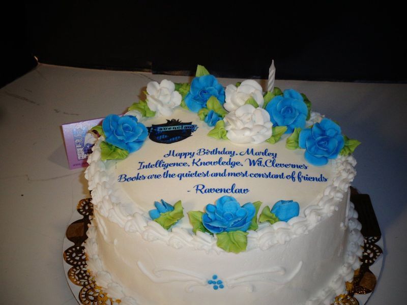 Birthday cake with blue and white floral frosting, message, and a lit candle.