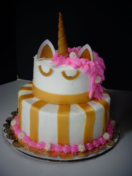 Two-tiered unicorn cake with gold accents, pink mane, daisy decorations, and closed-eye design.