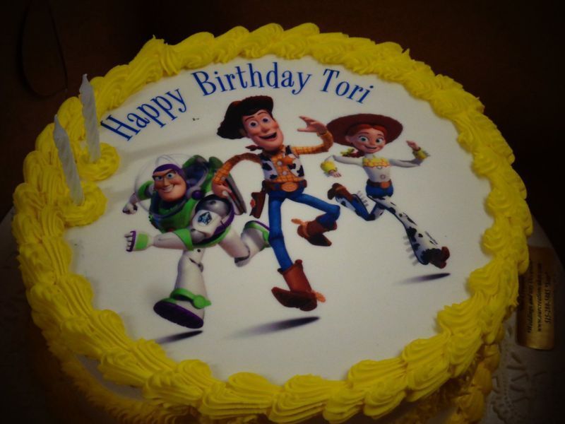 Toy Story birthday cake with Buzz Lightyear, Woody, and Jessie. Yellow frosting border; blue text.
