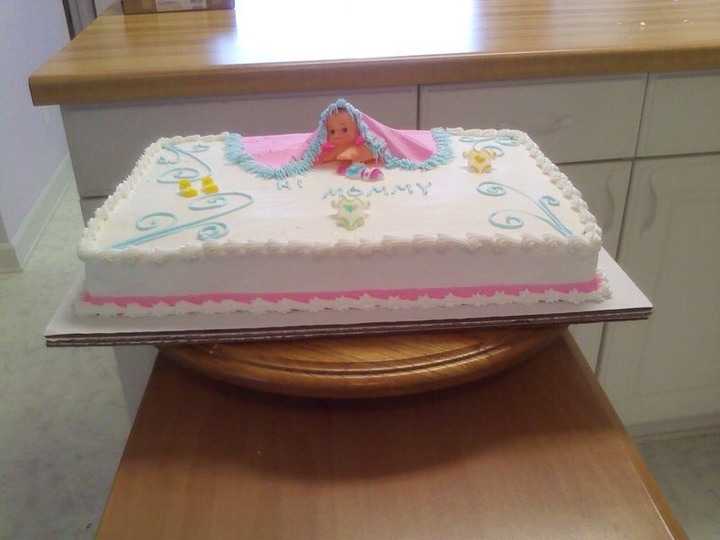 Baby shower cake with pink and blue frosting, a baby figurine, and decorative swirls.