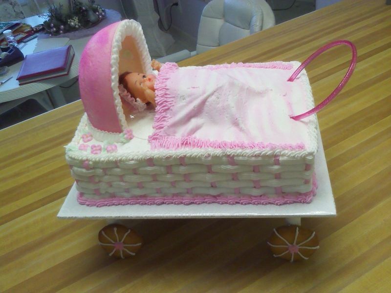 Pink and white baby carriage cake with a doll inside, set on a wooden table.