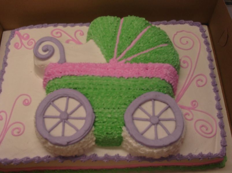 Cake decorated with a baby carriage in green, pink, and purple, on a rectangular cake with decorative swirls.