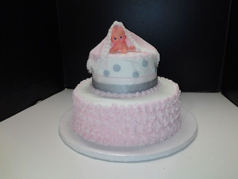 Two-tiered baby shower cake. Bottom tier is pink, top tier is white with a baby figurine on top.