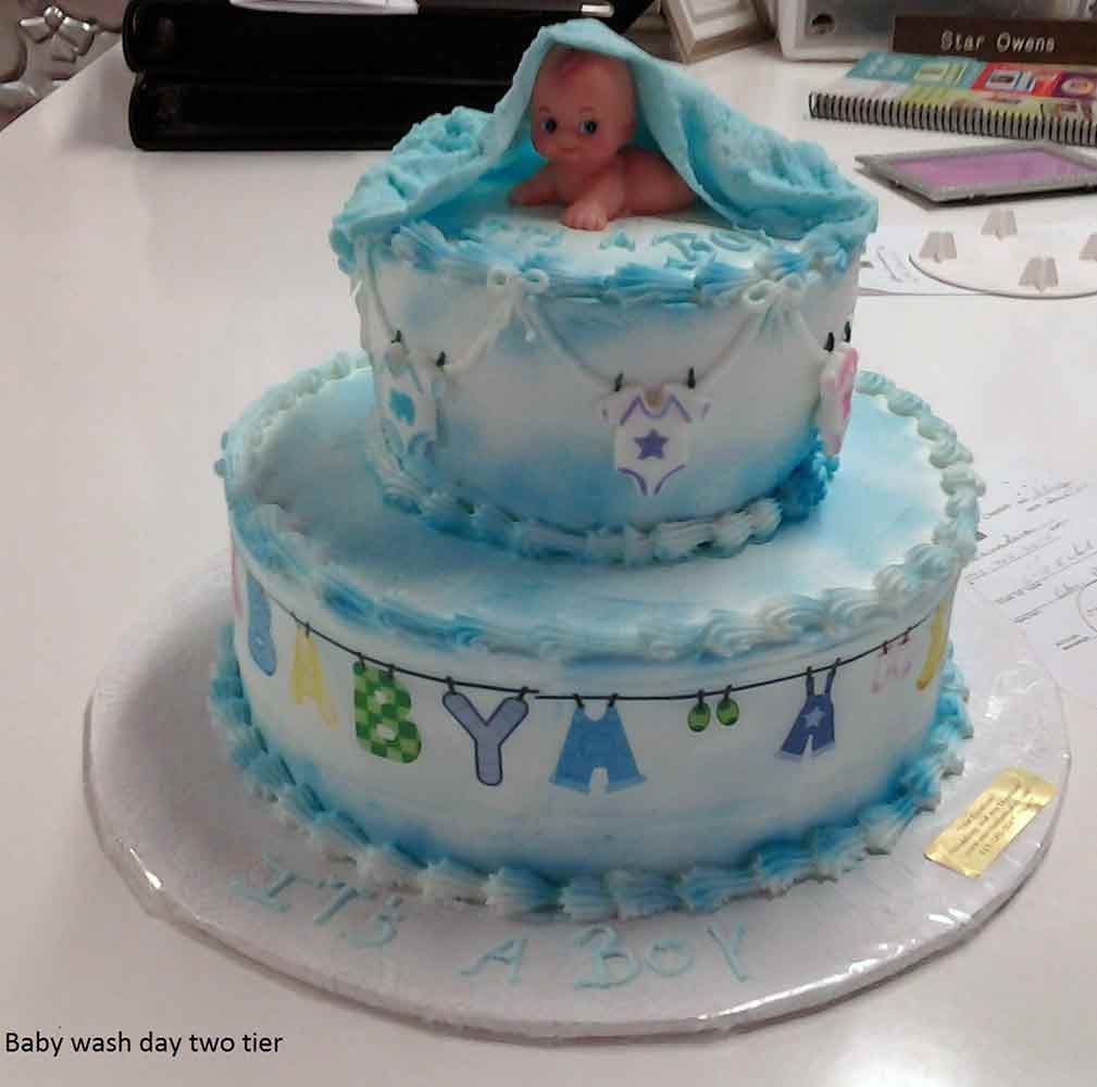 Two-tier blue baby shower cake with a baby figurine on top, decorated with clothesline and 