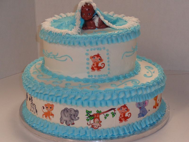 Two-tiered baby shower cake. Blue frosting, animal decorations, and a fondant baby.