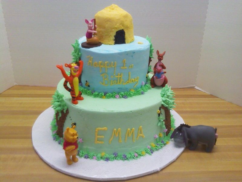 Two-tier Winnie the Pooh birthday cake with characters and a beehive, green and blue frosting, and 