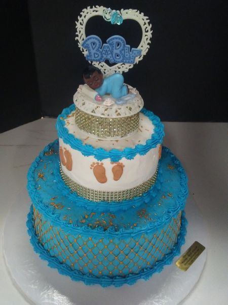 Three-tier blue and white baby shower cake with a baby figurine topper.