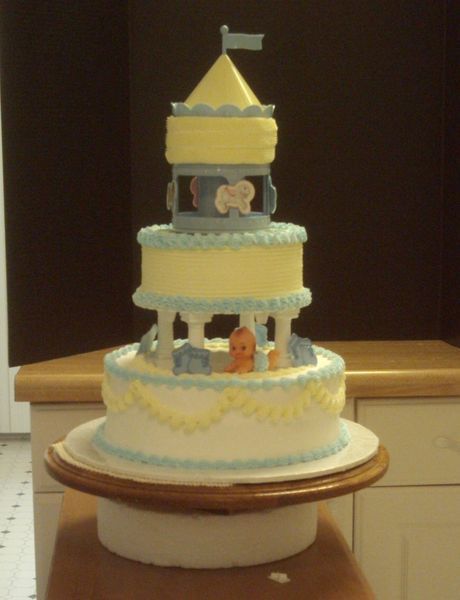 Carousel-themed cake with blue and yellow frosting, on a cake stand.