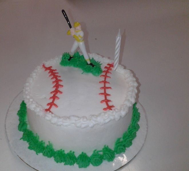 Baseball-themed cake with red stitches, green grass frosting, batter figurine, and a lit candle.