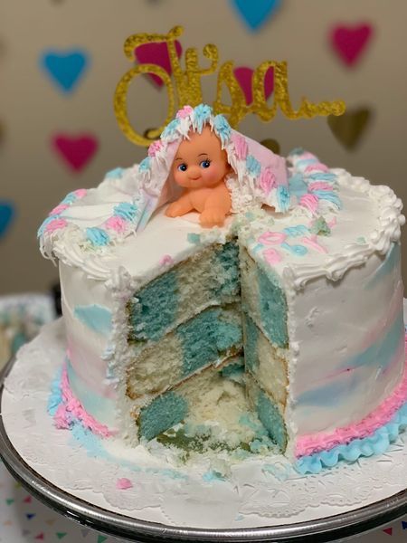 Gender reveal cake with blue and pink frosting, baby figurine, and gold 