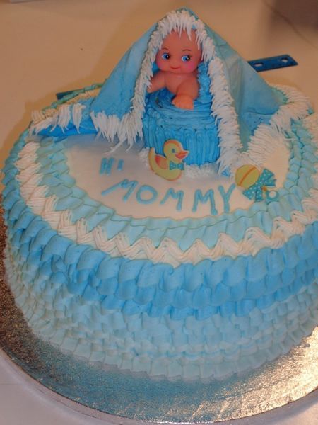 Blue and white baby shower cake with toy baby, blanket, and decorations. Reads 