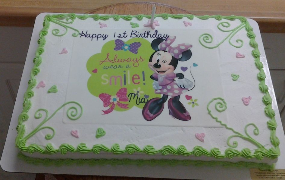 Rectangular cake with Minnie Mouse graphic, Happy 1st Birthday Mia text, green and pink accents.